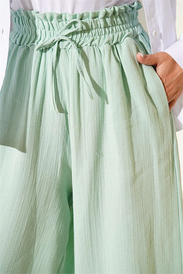 Loose-fitting muslin trousers with elastic waistband, light green.